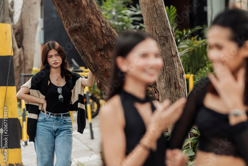 Fotografija A jealous young Southeast Asian woman secretly watches her girlfriend with another woman at the park, showing suspicion, envy, and possessive behavior