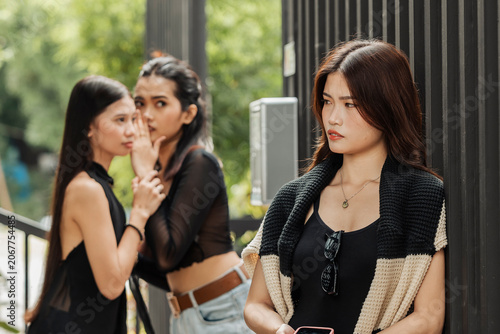 Φωτογραφία A young Southeast Asian woman looks uncomfortable as two women whisper behind he