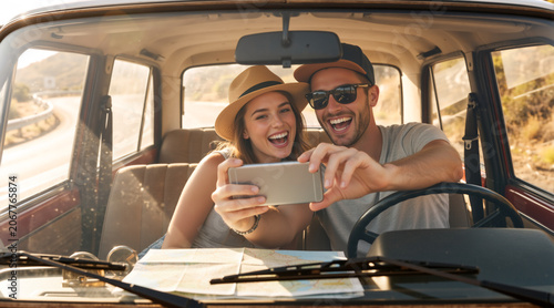 Young Caucasian couple taking a selfie with a smartphone inside a vintage car. Happy man and woman on a summer road trip with a map on the dashboard
