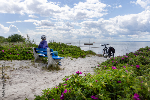 Woman cyclist wearing helmet sitting on blue bench by EuroVelo 10 R10 bike path on dunes in Hel, Poland