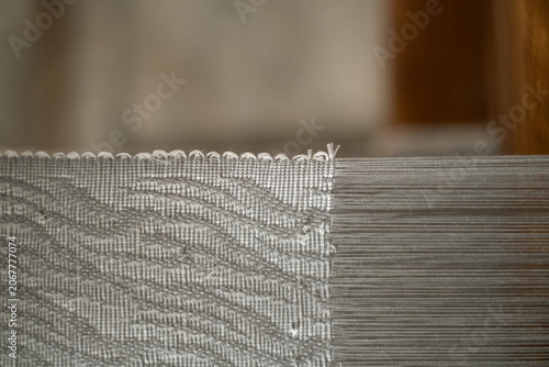 Fotografie Macro detail of the selvedge of beautiful grey wavy patterned tenun fabric connected to fine warp threads on a loom