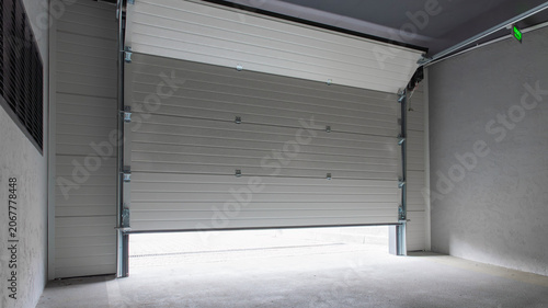 Fotografía Partially open white automatic sectional garage door in underground parking