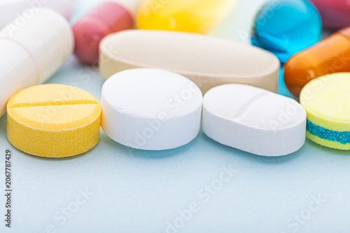 Photos Assorted tablets, capsules, and supplements arranged on a light blue background in a close up view
