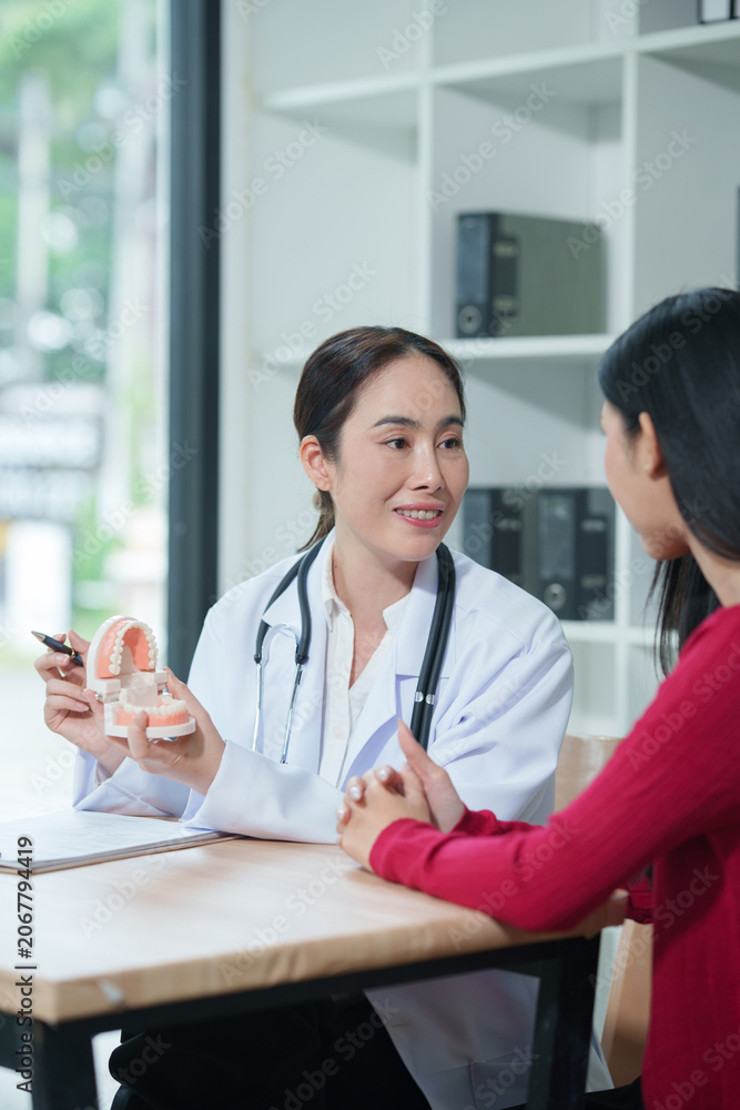 Fototapeta premium Female dentist explaining oral healthcare to patient using teeth model