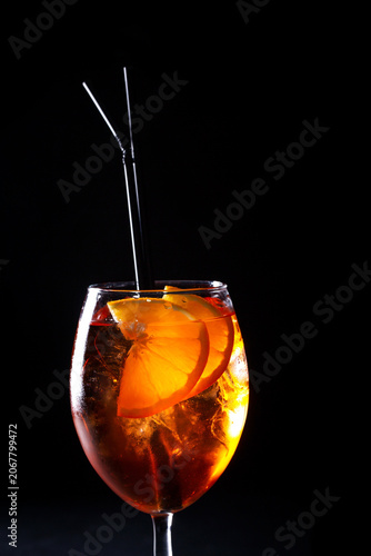 Refreshing cocktail with orange slices and ice in a glass on black background