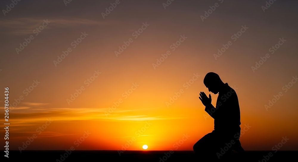 Fototapeta premium Silhouette of a man kneeling and praying to god during a sunset sunrise