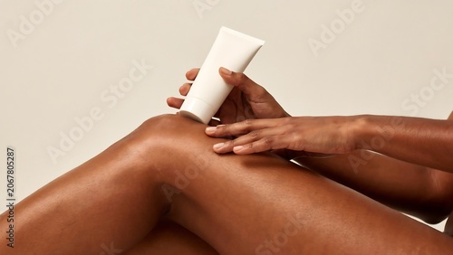 Woman applying white cream to her leg on beige background