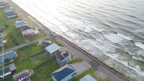 Coastal stilt homes Surfside Beach corridor along Seashell Dr presents elevated housing beside rock lined edge facing ocean view Gulf approach. Sunlit roofs, bright surf shimmer in Freeport, Texas