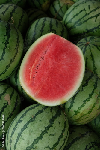 watermelon slices on top of a pile of watermelons at a fruit stand.