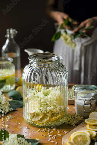 Preparation of elderberry flower syrup, ingredients and accessories visible on the table,  soft light with deep shadows.