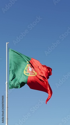 Big flag of Portugal fluttering in the wind on a white flagpole. Captured during a bright sunny day near Edward VII Park in Lisbon. Medium low angle shot. Vertical Video