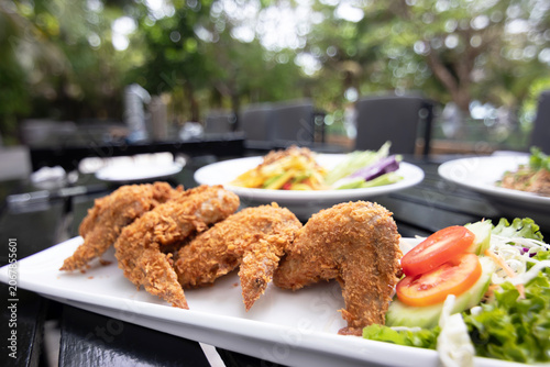 Fotografia Crispy fried chicken wing with fresh salad garnish on outdoor table, appetizing