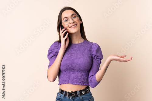 Young woman over isolated beige background keeping a conversation with the mobile phone with someone