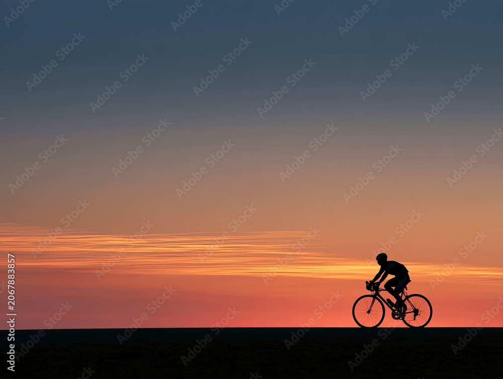 Fototapeta premium Silhouette of Person Cycling on a Road during Vibrant Sunset Sky
