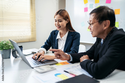 A woman and a man are sitting at a desk with a laptop and papers