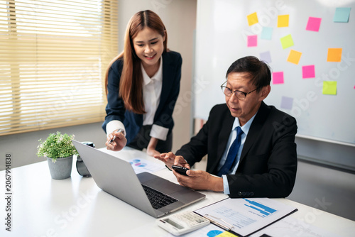 A woman and a man are sitting at a desk with a laptop and a cell phone