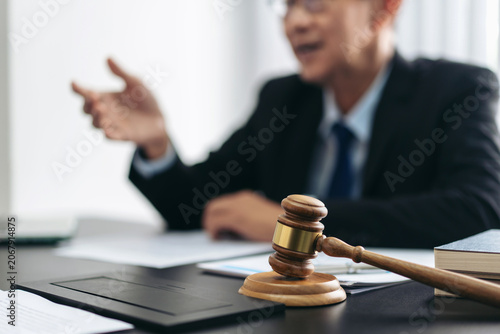 A man in a suit is sitting at a desk with a gavel and a stack of papers