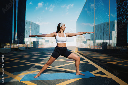 Foto Confident woman holding warrior pose, centered on mat, arms fully extended, aligned with city symmetry, showing mental strength, body tone, and flow of mindful digital movement