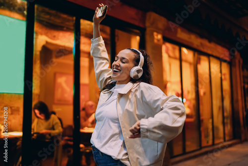 Billede på lærred Woman in headphones dances with raised arm, eyes closed, immersed in rhythm
