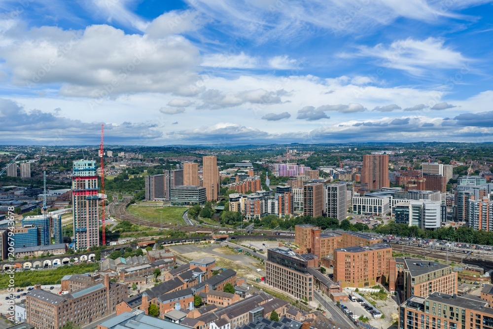 Obraz premium Aerial view of Leeds city centre showing South Bank regeneration railway lines modern residential towers commercial buildings and ongoing construction beneath a dramatic blue sky on a summer day