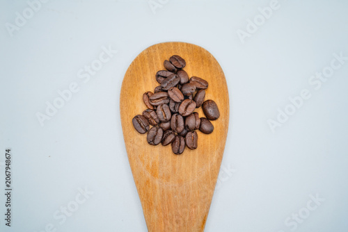 Small pile of roasted coffee beans inside a large wooden spoon flat lay.