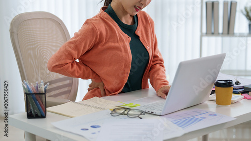Canvas-taulu Asian woman experiencing back pain while working on laptop at modern office desk