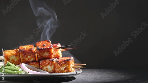 Hot and smoky paneer tikka skewers served with green chutney on a dark background