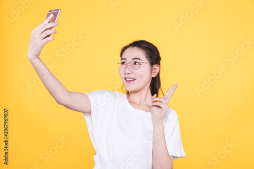 Bild auf Leinwand Smiling young woman taking selfie with smartphone on yellow background