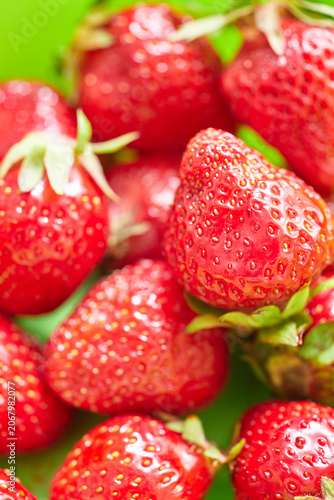 Macro shot of red strawberries in a green plastic bowl.