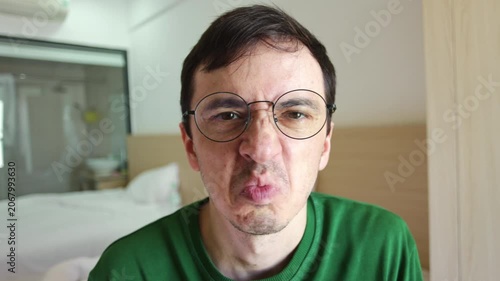 Man with glasses showing a strong negative emotion, wrinkling his nose and pursing his lips in revulsion as he looks directly at the camera, portraying a feeling of utter disgust