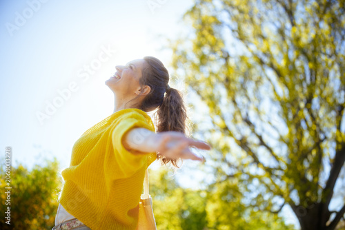 A woman in profile smiling toward the sun in a vibrant spring park, embodying serenity, mindfulness, and healthy living.