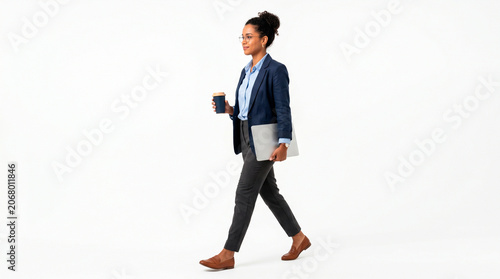 Professional woman in business attire walking with laptop and coffee cup on white background