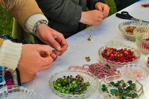 People making handmade jewelry at an outdoor master class. Hands stringing colorful beads from glass bowls, creative craft workshop.