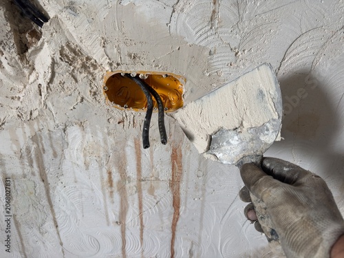 Worker smoothing plaster over electrical wires and box