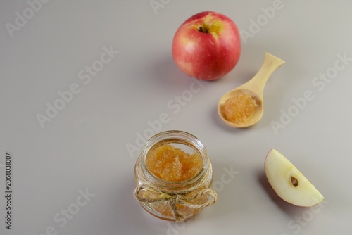 Apple jam in glass jar with apple slices and spoon on light background