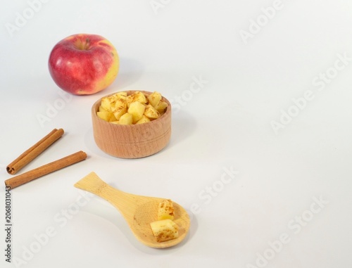 Apple pieces with cinnamon in wooden bowl and spoon on white background
