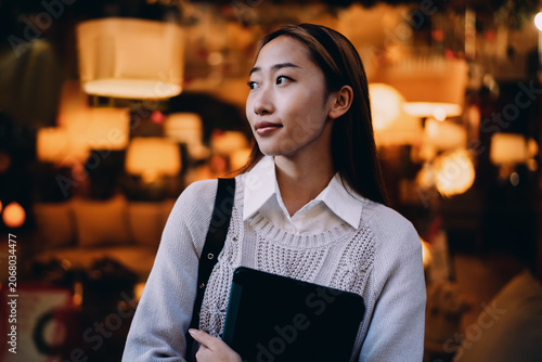 Photos Asian woman looking sideways with tablet under arm, suggesting thoughtful pause and connection to ideas in digital freelance space