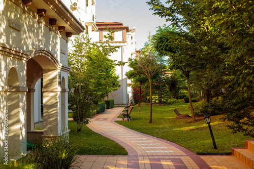 Cuadro en lienzo A curved brick pathway leads past a tan hotel building with archways toward a be