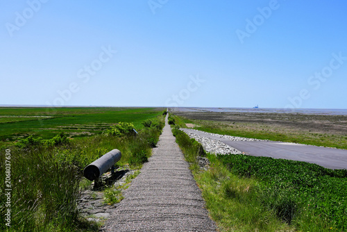 A scenic view along the empty paved pathway of the famous Trischendamm protection dike in Friedrichskoog, Germany, stretching into the endless horizon of the Wadden Sea mudflats
