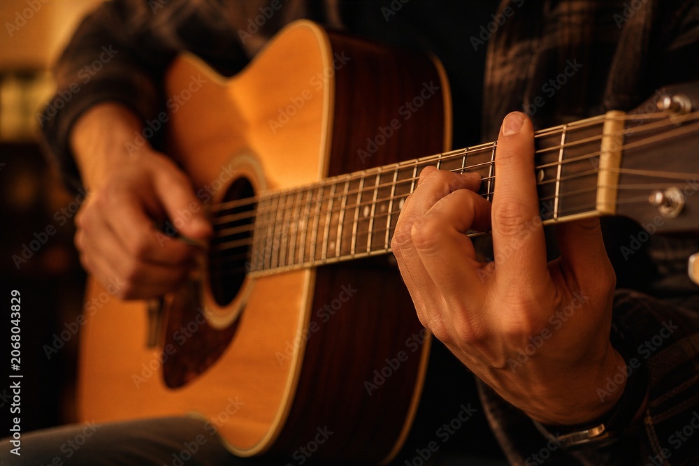 Fototapeta premium Person playing acoustic guitar in warm interior setting