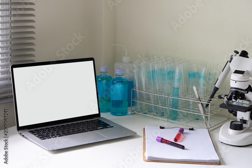 A side-angle view of a laboratory workbench displaying a blank laptop mockup, test tubes, and scientific equipment.