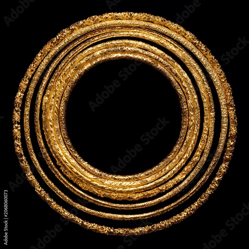Ancient Gold Bangles: A collection of intricately designed ancient gold bangles, stacked in a circular pattern against a stark black background.