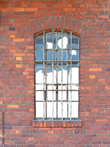 An old window with metal bars in a red brick building with broken windows. The building's interior is isolated.