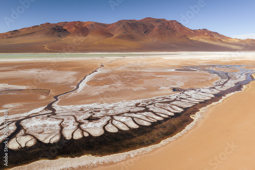 Aerial view of La Pacana caldera featuring intricate salt crust patterns and winding water channels set against arid desert mountains in San Pedro de Atacama, Antofagasta, Chile.