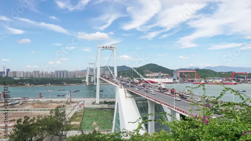 Busy Suspension Bridge Over Coastal Harbor with City Traffic and Blue Sky