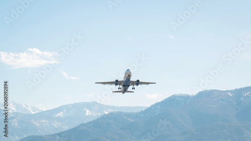 Passenger airplane climbing above mountain landscape with snow covered peaks under clear blue sky, dynamic aviation travel scene capturing departure, freedom, transportation, tourism, 