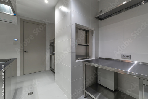 A kitchen space features stainless steel work surfaces with simple design. Walls are light and smooth. A door leads to another area. The space is bright and orderly