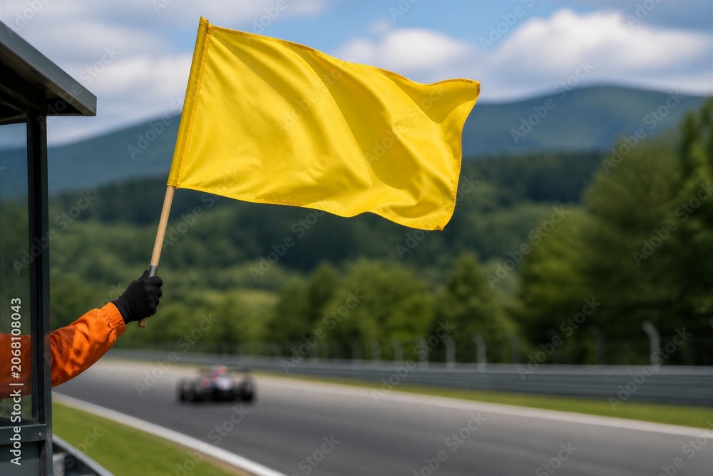 Naklejka premium Yellow flag waves above track. Hand grips pole with black glove. Orange sleeve hints at safety officer. Race car speeds below on asphalt. Green hills frame blurred background