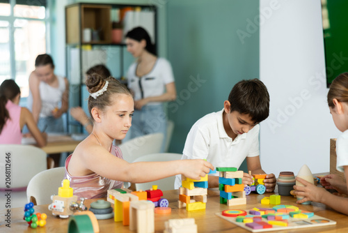 Tablou pe pânză In childrens leisure club, preteens play at table, they stack pyramids, solve puzzles, construct, play with wooden cubes