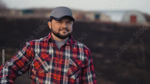 Countryman standing in farmland, medium portrait in nature, agribusiness. Joyful farmer correcting cap on head and admiring beautiful natural landscape in ecological region, innovation in agriculture